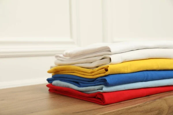 Sorting and organizing. Stack of different folded clothes on wooden table near white wall, closeup with space for text