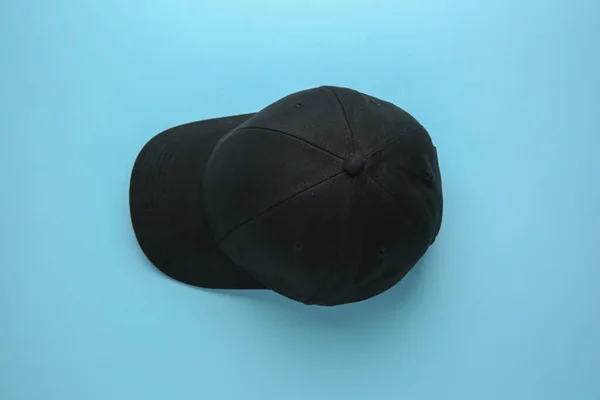 Stylish black baseball cap on light blue background, top view