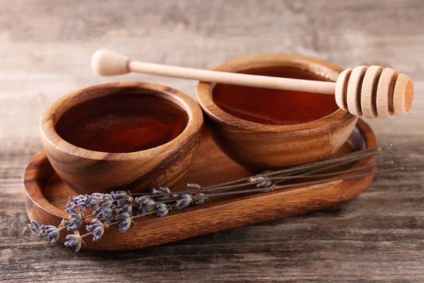 Delicious honey in bowls, lavender flowers and dipper on wooden table