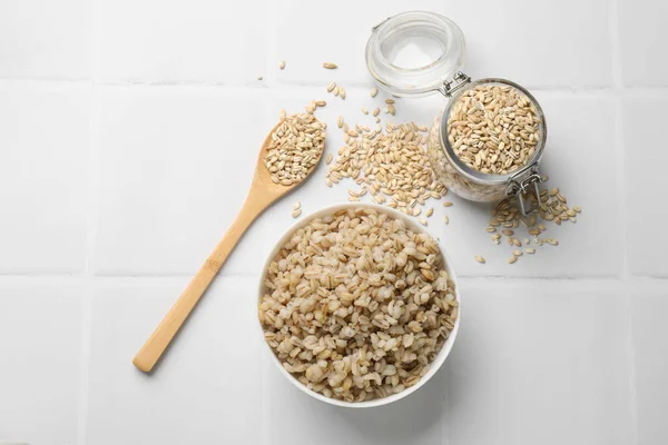 Delicious pearl barley served on white tiled table, flat lay