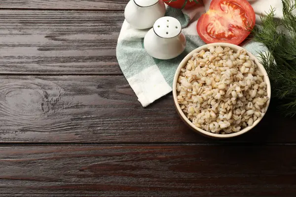 Delicious pearl barley in bowl served on wooden table, top view. Space for text