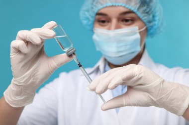 Şırıngayı cam şişeden alınan ilaçlarla dolduran doktor açık mavi arka plan, seçici odak