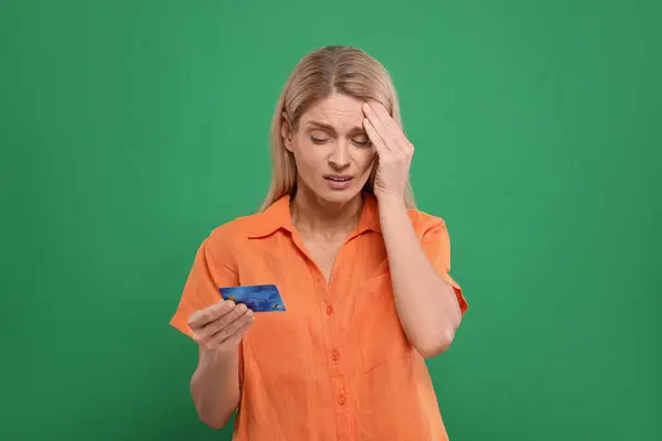 Stressed woman with credit card on green background. Be careful - fraud