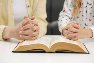 Kız ve vaftiz ebeveyni kapalı bir masada birlikte İncil için dua ediyorlar.