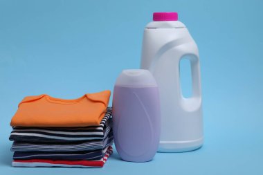 Açık mavi arka planda bebek kıyafetleri ve çamaşır deterjanı yığını