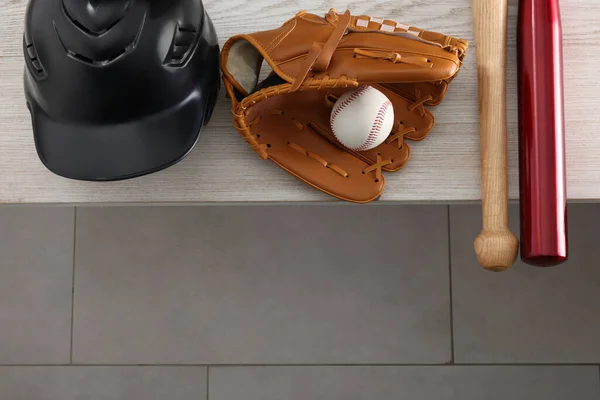 Baseball bats, batting helmet, leather glove and ball on wooden bench indoors, above view. Space for text