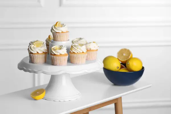 Delicious lemon cupcakes with cream and lemons in bowl on white table indoors
