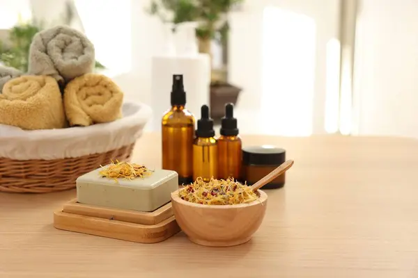 Soap bar, dry flowers, bottles of essential oils, jar with cream and towels on wooden table indoors, space for text. Spa time