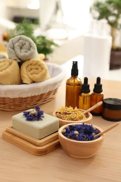 Soap bar, dry flowers, bottles of essential oils and towels on wooden table indoors. Spa time