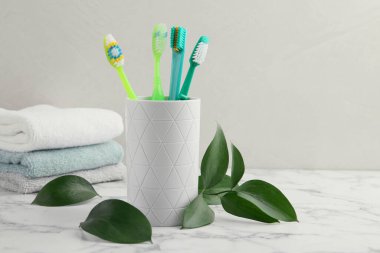Konteynırda renkli plastik diş fırçaları ve beyaz mermer masa üzerinde yeşil yapraklar, metin için boşluk
