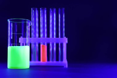 Koyu mavi arkaplanda parlak sıvılar bulunan laboratuvar camları, metin için boşluk