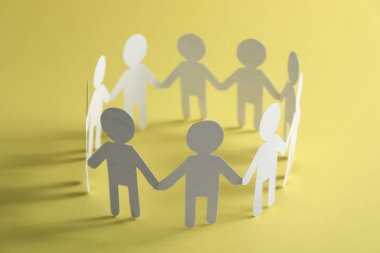 Takım çalışması konsepti. Sarı arka planda el ele tutuşan insanların kağıt figürleri.