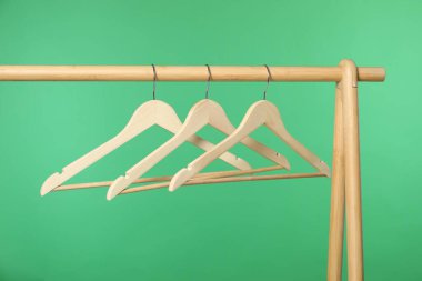Boş elbiseler, ahşap askılarda yeşil arka planda asılı.