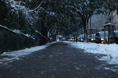 Şehir caddesi karla kaplı, alçak açılı.