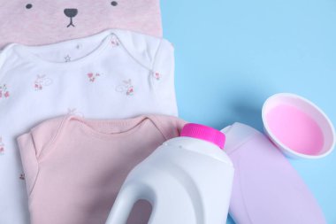 Çamaşır deterjanı ve açık mavi arka planda bebek kıyafetleri, düz yatış. Metin için boşluk