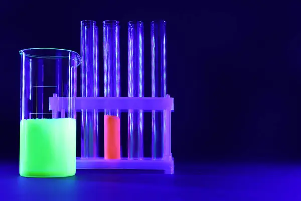 Laboratory glassware with luminous liquids on dark blue background, space for text