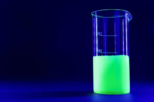 Laboratory beaker with luminous liquid on dark blue background, space for text