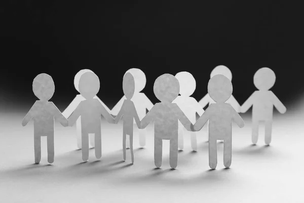 Teamwork concept. Paper figures of people holding hands on white table, closeup