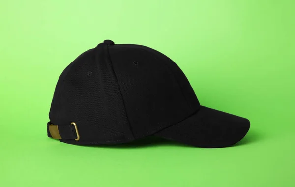 Stylish black baseball cap on light green background