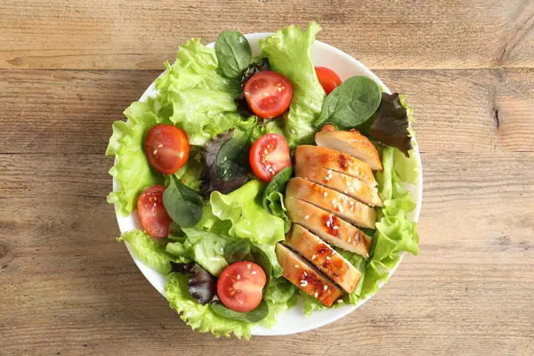 Delicious salad with chicken, cherry tomato and spinach on wooden table, top view