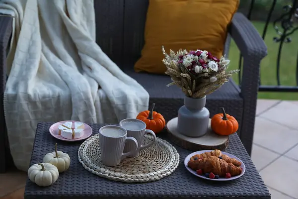 Rattan table with cups of drink, croissants, cheese and autumn decor on terrace