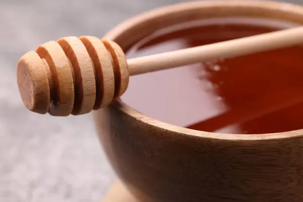 Delicious honey in bowl and dipper on grey table, closeup