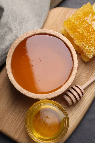 Sweet honey in bowls, dipper and pieces of honeycomb on grey table, flat lay