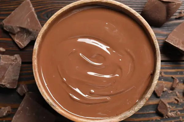 Tasty milk chocolate paste in bowl and pieces on wooden table, top view