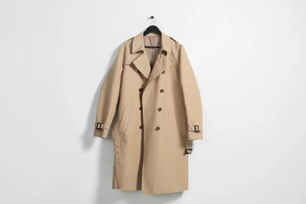 Hanger with beige trench coat on white wall
