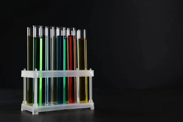 Many test tubes with liquids in stand on black background, space for text