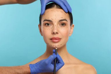 Açık mavi arkaplanda estetik ameliyat için kalem hazırlayan bir doktor.