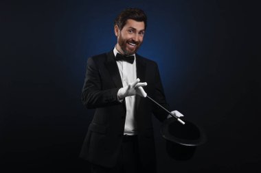 Mutlu sihirbaz koyu mavi arka planda silindir şapkalı sihirbazlık numarası yapıyor.