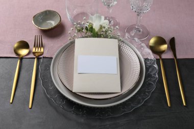Masa dekorları çok şık. Tabaklar, çatal bıçak takımı, boş kart ve çiçek dekoru.