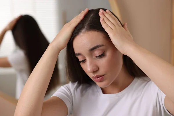Woman examining her hair and scalp indoors