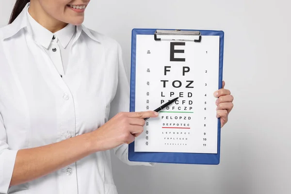 Ophthalmologist pointing at vision test chart on light background, closeup