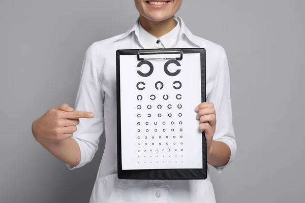 Ophthalmologist pointing at vision test chart on gray background, closeup