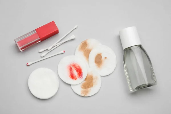 Bottle of makeup remover, cotton pads, buds and lipstick on light grey background, flat lay