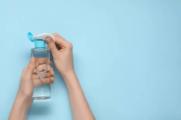 Woman pouring makeup remover onto cotton pad on light blue background, top view. Space for text