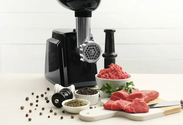Meat grinder, beef, parsley and spices on white table