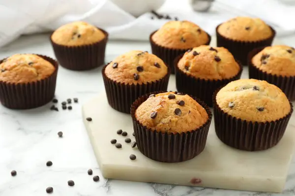 Delicious sweet muffins with chocolate chips on white marble table, space for text
