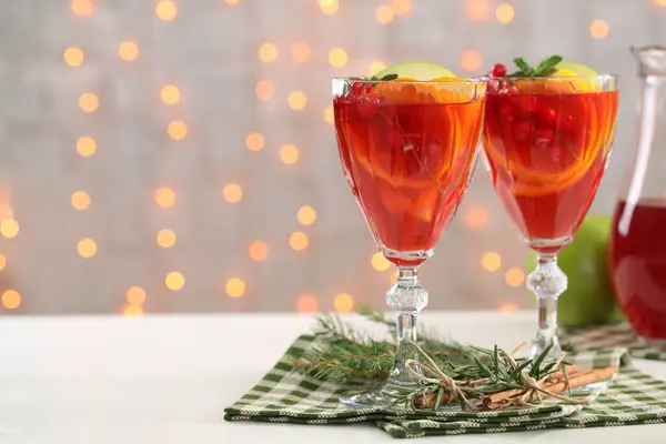 Christmas Sangria cocktail in glasses, cinnamon sticks and fir tree branch on white table against blurred lights. Space for text
