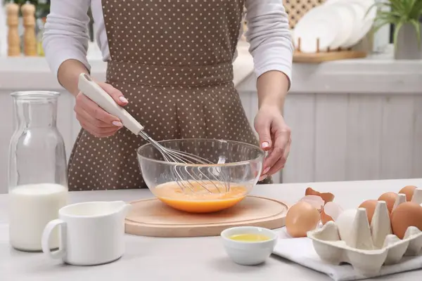 Woman whisking eggs in bowl at table indoors, closeup