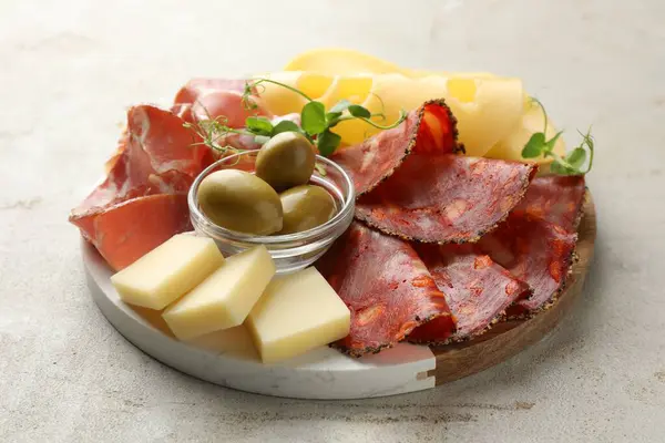 Serving board with delicious cured ham, cheese, sausage and olives on light table