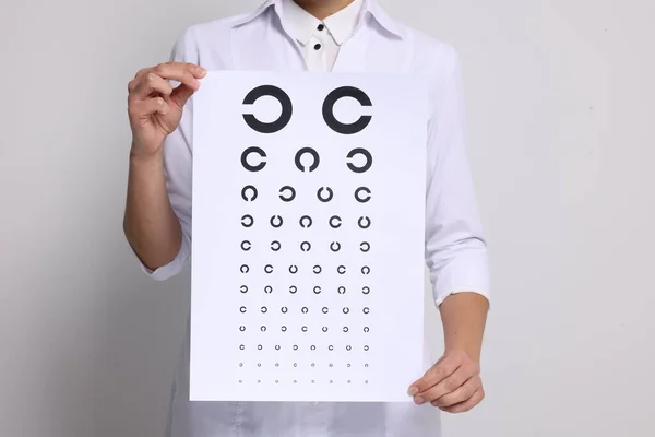 Ophthalmologist with vision test chart on light background, closeup