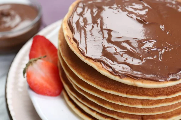 Tasty pancakes with chocolate paste and strawberries on table, closeup