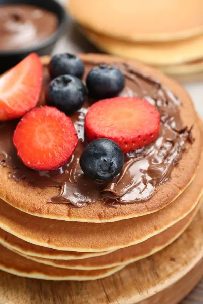 Tasty pancakes with chocolate paste and berries on table, closeup