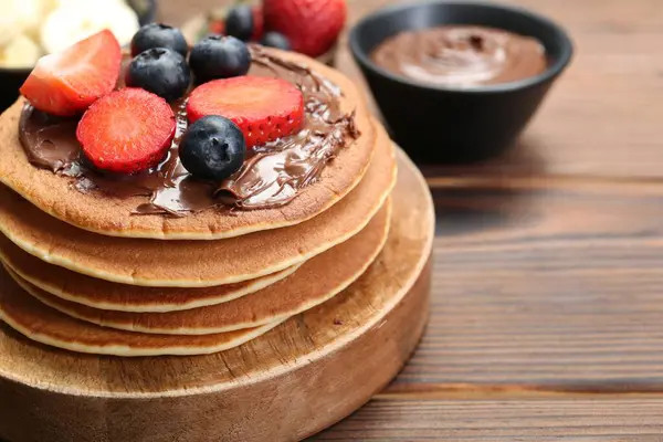 Tasty pancakes with chocolate paste and berries on wooden table, closeup. Space for text