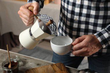 Moka pot 'tan bardağa aromatik kahve döken adam mutfaktaki masada, yakın plan.