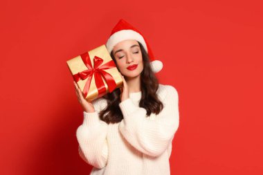 Kırmızı arka planda Noel hediyesi olan Noel Baba şapkalı güzel bir kadın.
