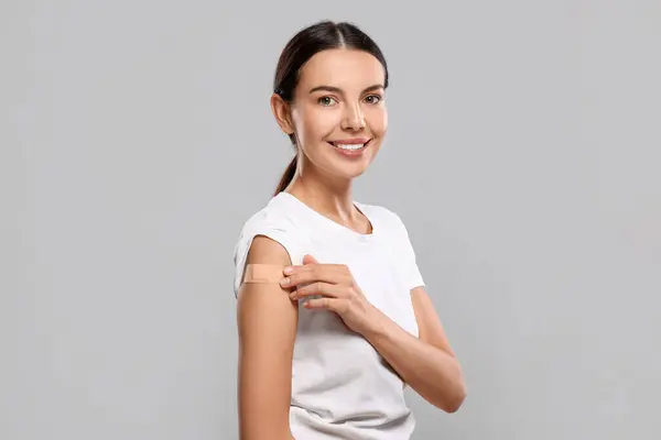 Woman with sticking plaster on arm after vaccination against light grey background